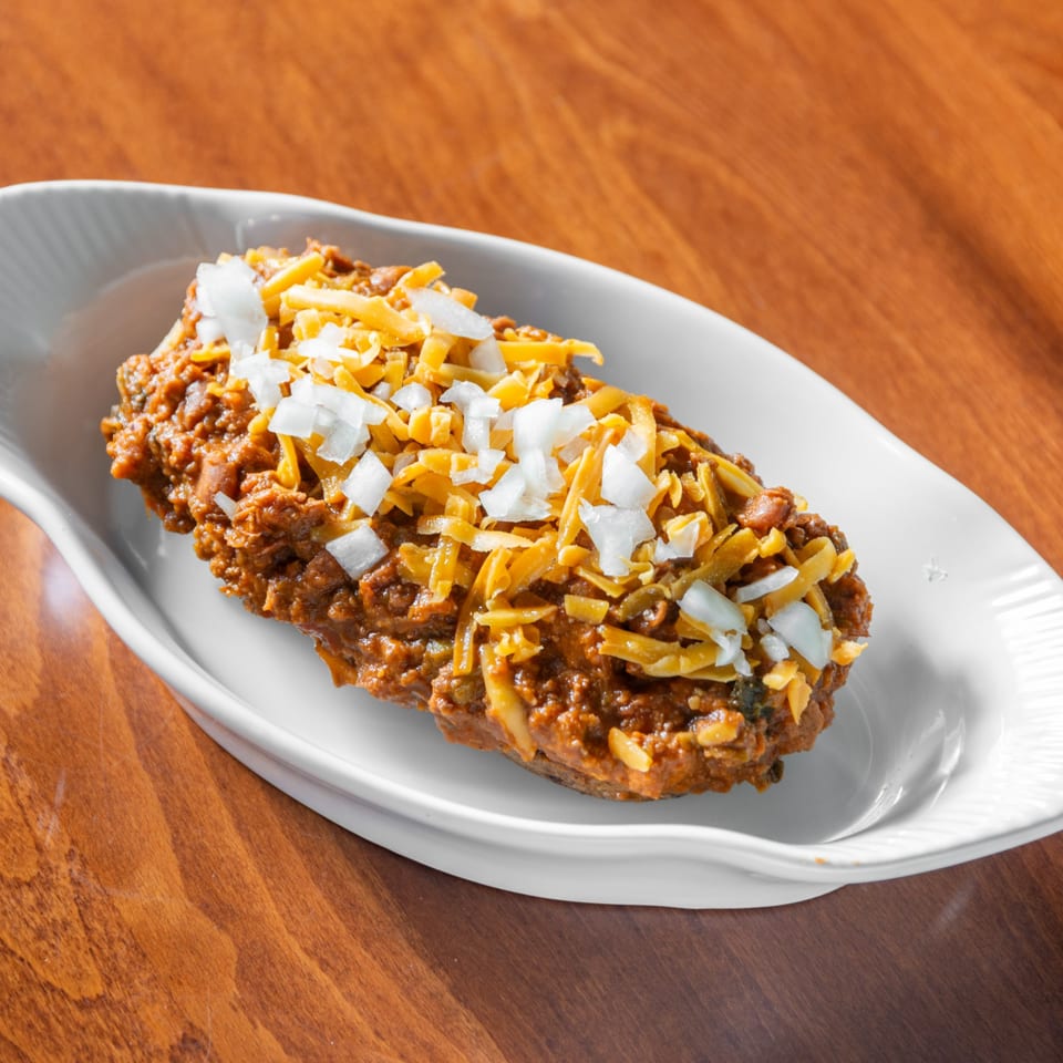 Brownsville Deli's chili dog, topped with shredded cheese and diced white onions, in a white dish.