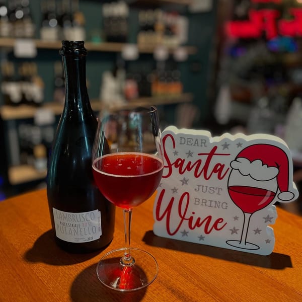 A bottle of Lambrusco Ancestrale Rose wine next to a glass of red wine and a festive sign.