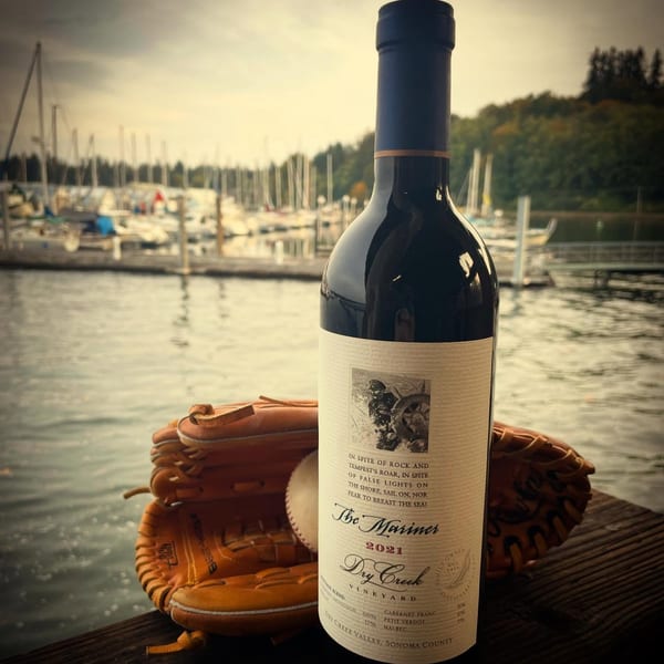 A bottle of "The Mariner" wine, a baseball glove, and a baseball on a dock overlooking a marina.
